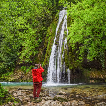 Back view of male traveler photographing scenic mossy waterfall