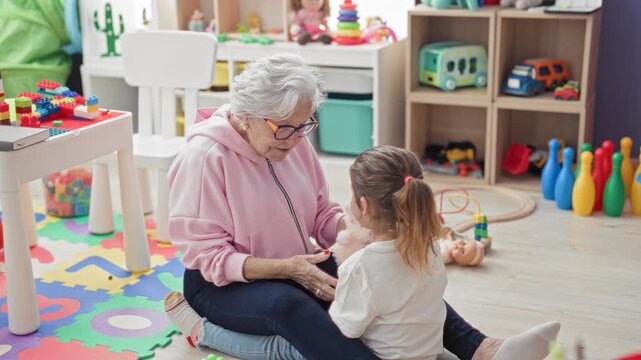 Elderly woman reaches arms to hug little girl on a toy strewn playmat inside a building; affection bonding.