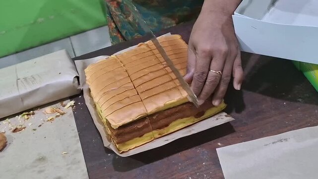 A hand holds a knife and cuts a square sponge cake. Fresh oven baked and sliced sponge cake with knife. Pineapple chocolate original home made cake for bakery seller. 