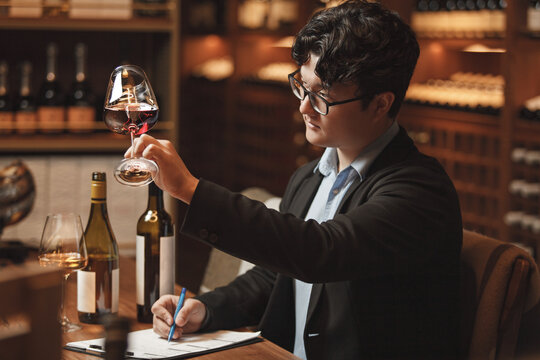 Professional Sommelier Conducts Wine Tasting Session Sitting at Table in Cellar. 