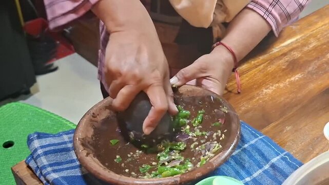 hands grind a bowl of chilli. making sambal from indonesia. Making Sambal using traditional tool, stone pestle and mortar.