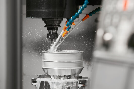 Milling machine drills holes on a metal part. CNC metalworking with coolant liquid. Industrial technologies concept.