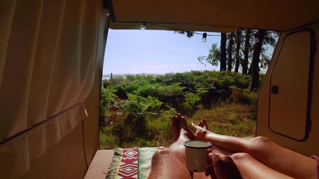 Couple's Legs Resting and Morning Coffee in Vintage Campervan with Fern and sea Forest View &ndash; Van Life Lifestyle