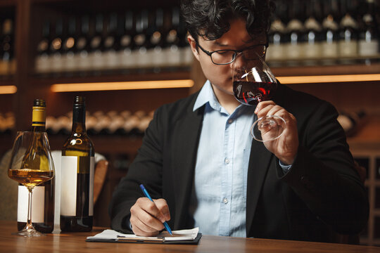 Sommelier Writing Notes With Glass of Wine Sitting at Table Being in Cellar