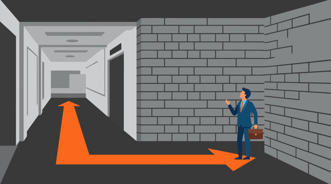Puzzled businessman in blue suit holding briefcase standing at dead-end brick wall after following misleading orange painted arrow through empty office corridor, concept of wrong direction, failed