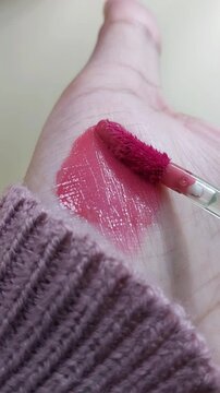 Process of showing red lip tint color on palm using beauty brush applicator. Vertical close up shot. Lip product swatch for cosmetic presentation.
