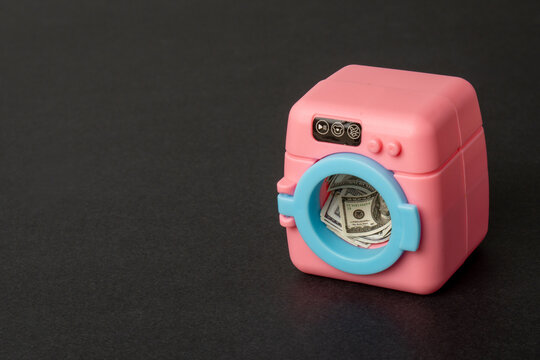 Toy washing machine filled with US dollar bills. Money laundering, financial crime, illegal currency cleaning, tax evasion concept. Copy space for text.