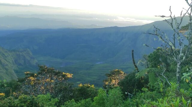 Majestic sunrise over an expansive mountain valley, revealing a breathtaking natural landscape with lush greenery and distant peaks under a soft, ethereal sky