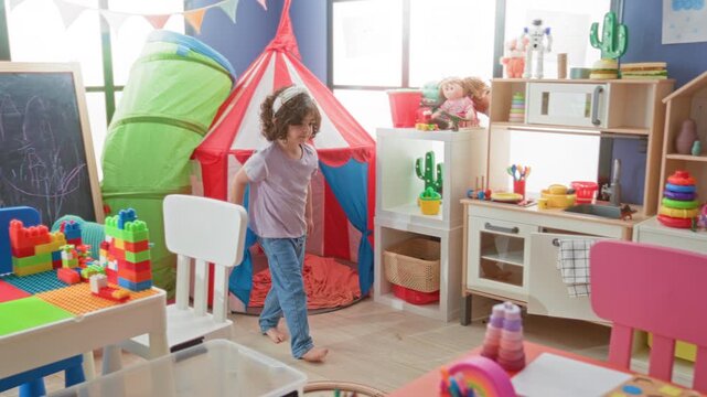 Girl bending to pick up a toy car near storage shelves and stacking rings in building playroom; playful curiosity.