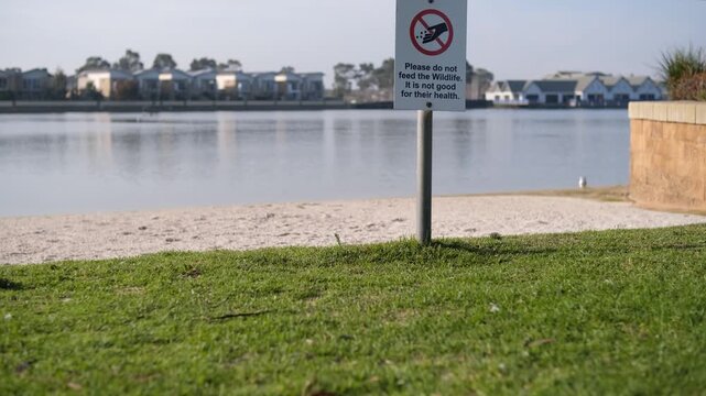 A public advisory sign reads "Please do not feed the Wildlife. It is not good for their health" in Sanctuary Lakes near waterfront houses. Point Cook, suburb of Melbourne, Australia. 