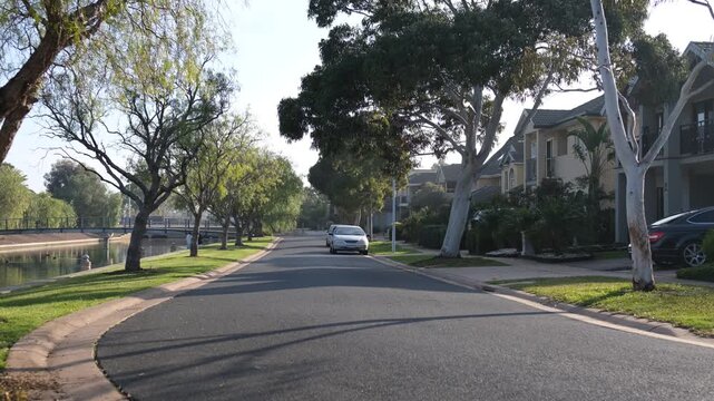 A quiet residential street with houses and neat nature strip running parallel to a calm canal or waterway in Sanctuary Lakes, suburb of Point Cook, Melbourne, Australia. 