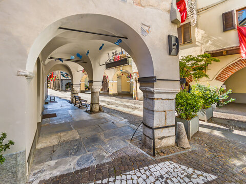 Medieval arcades along Contrada Mondovi in the old town of Cuneo, Piedmont, Italy. Pedestrian street features ancient stone vaults, low massive pillars, traditional cobblestone flooring