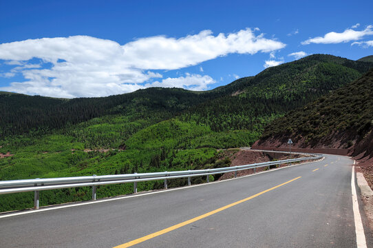 Scenic winding road through lush green mountainous area under clear blue sky