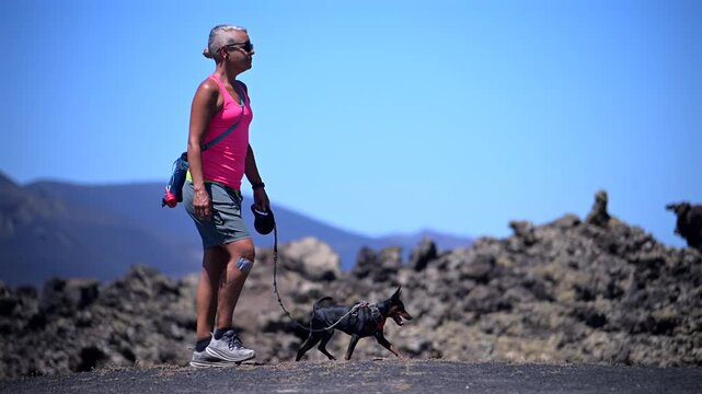Female Hiker Trekking with a Miniature Pinscher Dog Along a Volcanic Trail in the Lanzarote Badlands