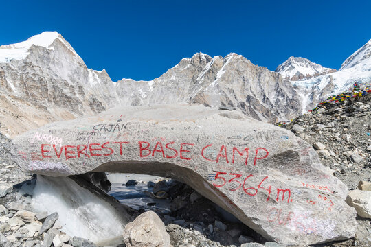 A large glacier-polished boulder covered in visitors' graffiti reads 'Everest Base Camp 5364m,' with snow-covered Himalayan ridges stretching across the background