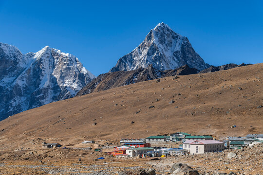 The remote high-altitude settlement of Lobuche spreads across a brown plateau, its colorful tin-roofed teahouses dwarfed by two sharp mountain peaks above.