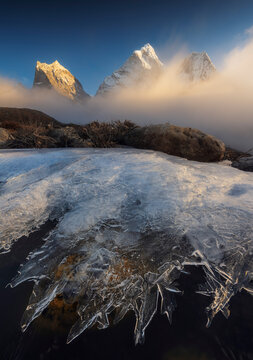 Frozen ice crystals in the foreground with snow-capped Himalayan peaks (Ama Dablam) emerging from morning mist, high altitude Everest region, Nepal.