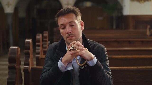 Private moment of prayer, a man sitting on a wooden pew in a peaceful, empty Christian church, praying with rosary beads.