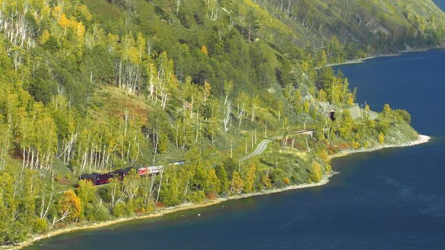 Red train traveling on the Circum Baikal Railway along the scenic coast of Lake Baikal, Russia
