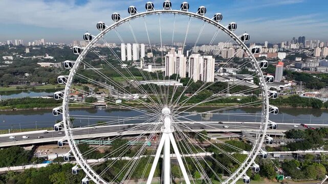 Cinematic drone zoom-out from the Ferris wheel at Villa-Lobos Park, revealing S&atilde;o Paulo's expansive skyline in the background. Beautiful sunny day with a vibrant blue sky. Aerial footage of a modern u