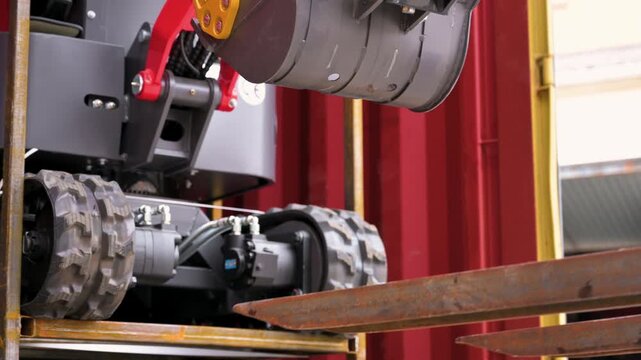 Close-up of rubber tracks and chassis of a mini excavator inside a red shipping container during unloading process. High quality 4k footage