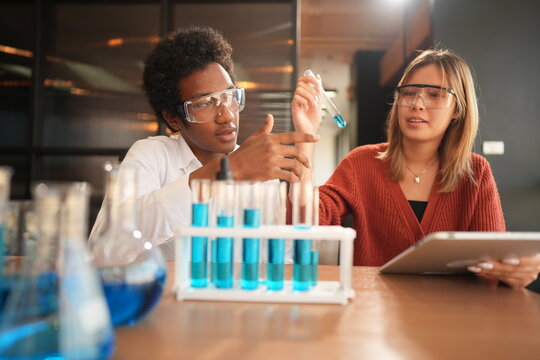 Two science students in a chemistry laboratory compares two test tubes of blue liquid with a classmate in a bright modern training studio, celebrating diversity and teamwork in learning