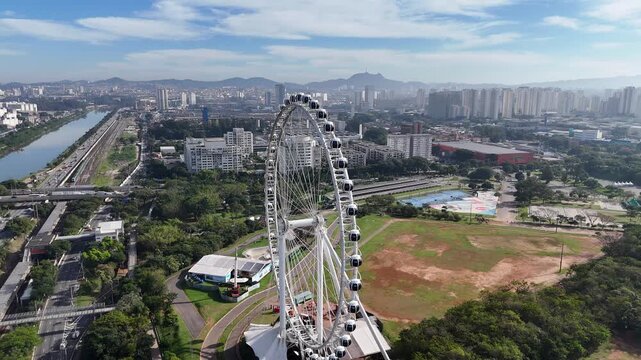 Cinematic drone pullback from the Ferris wheel at Villa-Lobos Park, revealing the Marginal Pinheiros and the expansive skyline of S&atilde;o Paulo, Brazil. Beautiful sunny day with a vibrant blue sky. Aerial