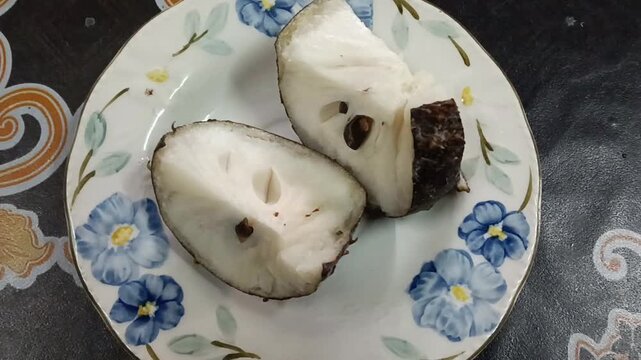Fresh soursop (durian belanda) cut into halves and served on a floral ceramic plate, revealing its soft white flesh and glossy black seeds. Soursop (Annona muricata) is a tropical fruit known for its 