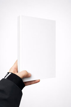 Close up of hand holding blank white hardcover book mockup against white background, template for cover design