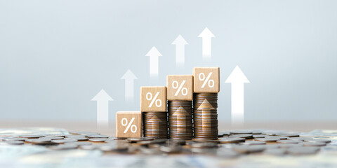 A wooden block image with percentage (%) symbols stacked on a pile of coins, with an upward-pointing arrow, reflects effective financial planning and increasing interest. © Wachirapong