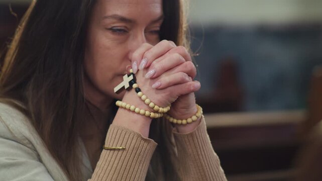 Woman with hands clasped in prayer, holding a Catholic rosary with a dangling cross. Concept of faith, devotion, and peaceful meditation.