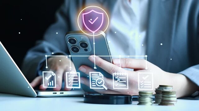 Business activity involving mobile phone with security icons and coins on a desk during daytime.