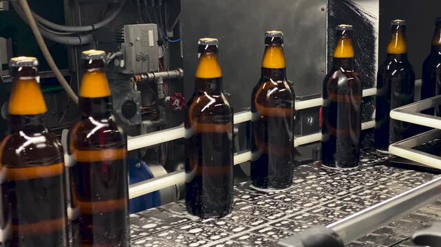 Amber beer bottles moving through an industrial brewery filling line with metal machinery and caps