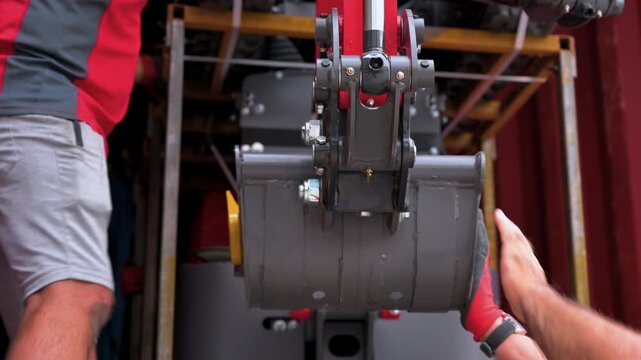 Professional workers manually guiding and checking a mini excavator digging bucket while unloading it from a container. High quality 4k footage