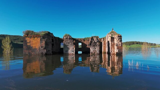 Aerial shot Saint Paul and Peter (Surb Pogos Petros) Church in Aparan Reservoir, Armenia. Ancient Armenian church partially submerged in the blue waters of Aparan Reservoir, Armenia. Historic medieval