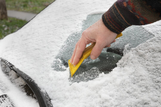 Winter scene, human hand scraping ice from windshield of car
