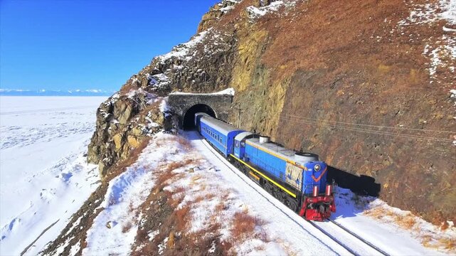 Aerial view of a train exiting a tunnel along the snowy coast of the frozen Lake Baikal in Siberia