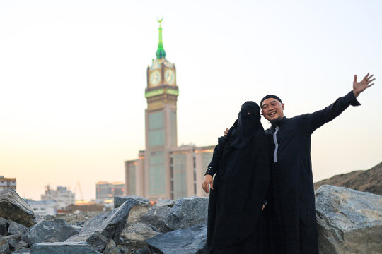 Happy Muslim Couple Poses On Rocky Hill With Clock Tower Blurred In The Background