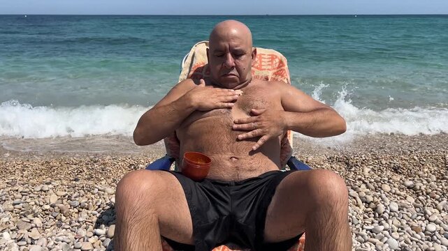 Hombre sentado aplicando crema solar en la playa