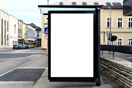 bus shelter at a busstop. blank billboard ad display. empty white lightbox sign. glass and aluminum frame structure. city transit station. bench inside. urban street setting. outdoor advertising