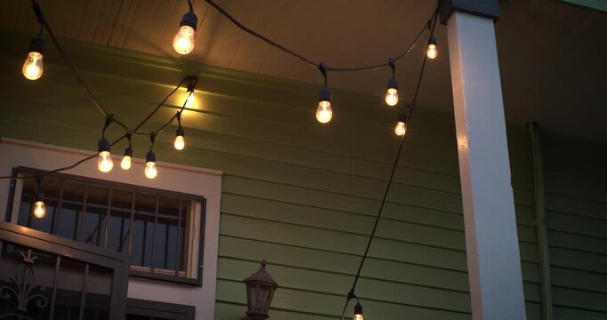 Warm string lights hanging above a New Orleans porch at dusk. Cozy residential exterior with a vintage atmosphere, glowing bulbs, and an inviting evening ambiance for lifestyle or hospitality themes.