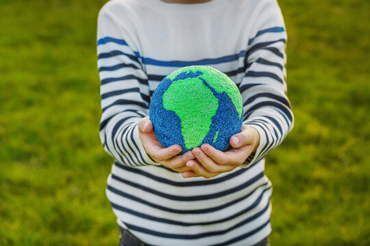 Authentic image featuring real people. Little hands tenderly hold a small globe, symbolizing care for the planet and a hopeful future, with soft light and a blue background