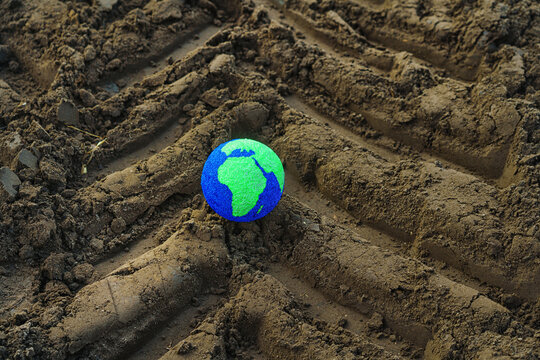 A small globe lies in a tractor track. Symbolizing care for the planet and a hopeful future. Industrialization or cultivation of the land.