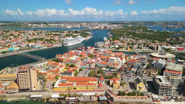 Aerial pullback shot reveals colorful Punda district in Willemstad Curacao with cruise ship docked along Sint Anna Bay near Queen Emma Bridge