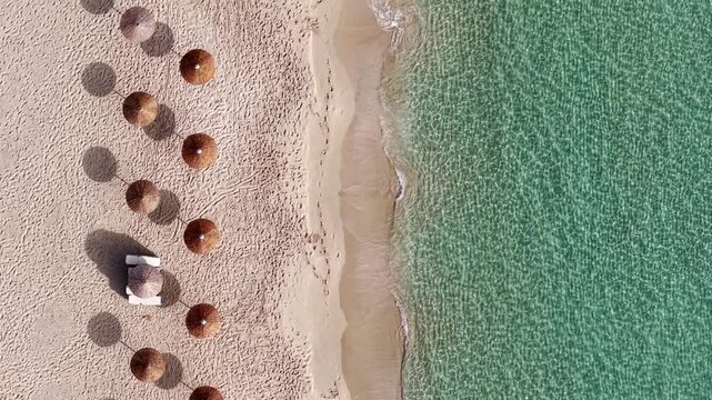 Straw umbrellas at beach on turquoise sea shore on a sunny day, Simos beach emerald green water, Elafonisos island, Overhead drone shot