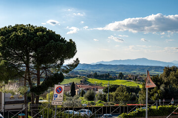 Obraz premium Panoramic view of the Tuscan countryside with a roadside overlook, distant hills, and a wide valley under a bright sky. The scene captures the beauty of rural Italy.