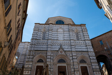 Fototapeta premium Low-angle view of Siena Cathedral with ornate white marble facade and decorative details. The perspective highlights the monument’s craftsmanship and grandeur.