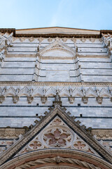 Fototapeta premium Close-up view of the ornate white marble facade of Siena Cathedral in Tuscany, Italy. The image highlights the intricate Romanesque and Gothic architectural details against a clear blue sky.