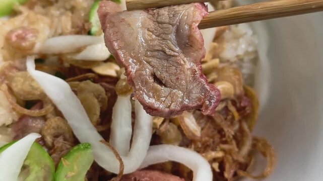 Close up of chopsticks holding a delicious slice of char siu pork over Vietnamese sticky rice with pickled vegetables