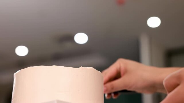 Pastry chef hands carefully spread frosting, smooths sweet cream icing with spatula for birthday bakery order in professional kitchen, cake spins slowly on turntable, baking, confectionery, culinary